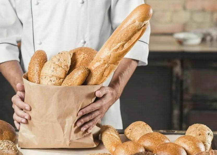 На фото повор-кулинар испекший свежий хлеб укладывает булки в пакет.