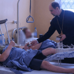 На фото священник в военном госпитале помогает раненым солдатам в специальной военной операции.