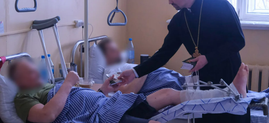 На фото священник в военном госпитале помогает раненым солдатам в специальной военной операции.