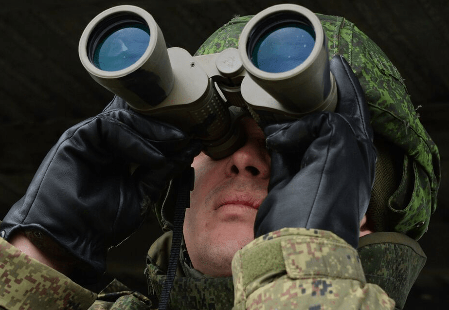 На фото военный солдат смотрит в оптику для наблюдения за врагом на большом удалении.